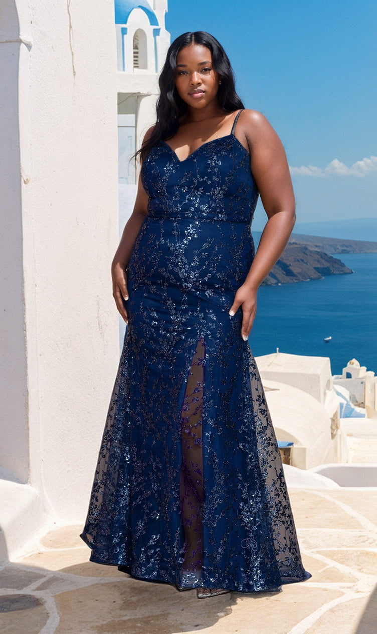 A woman in the Glitter Plus-Size Long Mermaid Prom Dress W1154, featuring navy blue sequins and a sleeveless, floor-length design, stands outdoors with white buildings and a blue sea in the background.